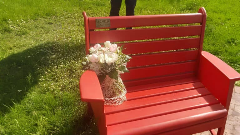 Una panchina rossa sul prato con un vaso di fiori bianchi