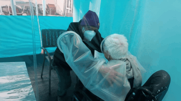 Un’operatrice con dispositivi di protezione abbraccia una persona anziana