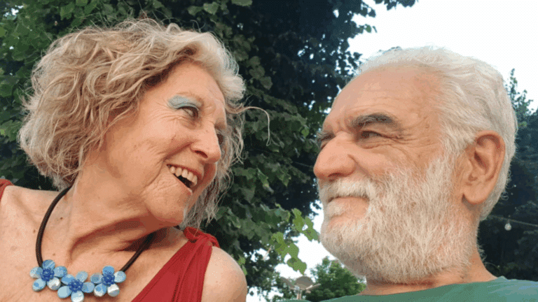 Una donna e un uomo dai capelli bianchi si guardano sorridendo all’aperto