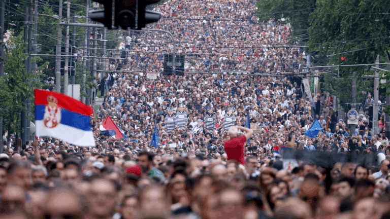 Una folla di manifestanti riempie una strada con bandiere serbe