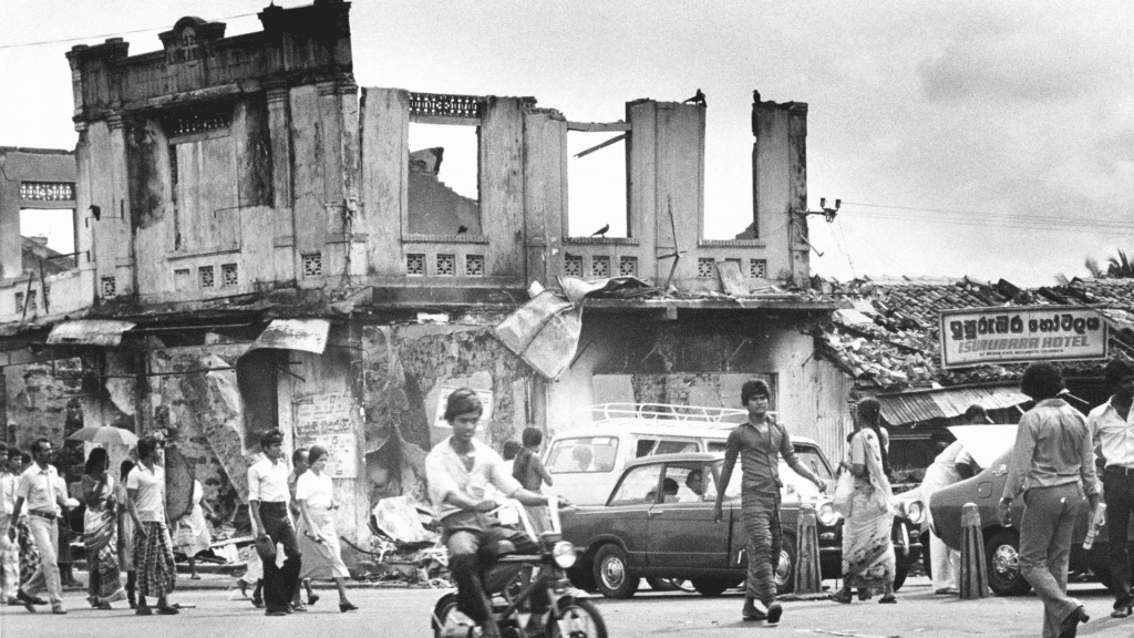 Gli abitanti della capitale Colombo, Sri Lanka, camminano tra i resti carbonizzati di un mercato dopo cinque giorni di rivolte e incendi, il 29 luglio 1983. 
La violenza anti-tamil causò centinaia di morti e distrusse edifici ed attività commerciali.