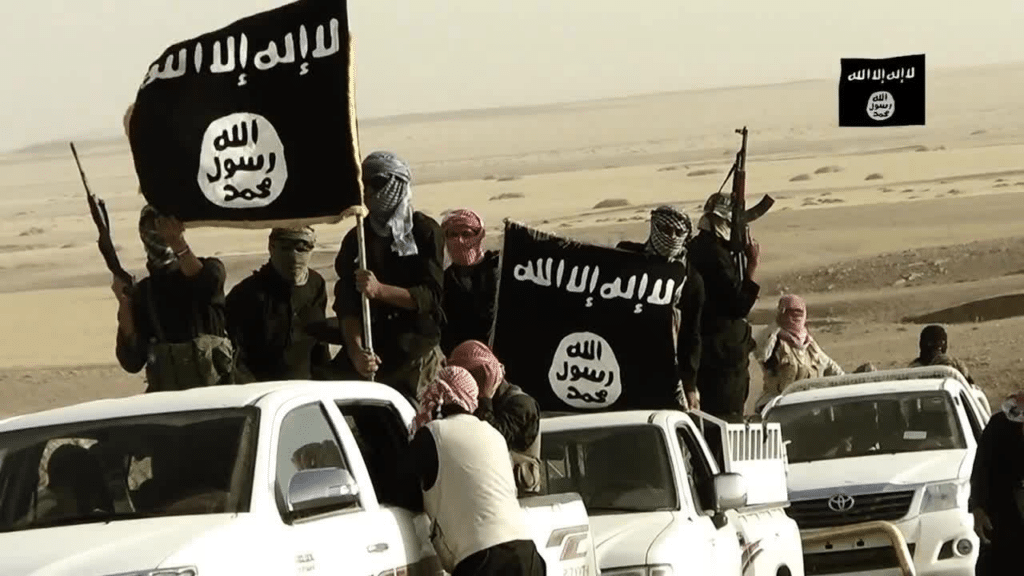Alcuni militanti dello Stato Islamico (IS) con la rispettiva bendiera.