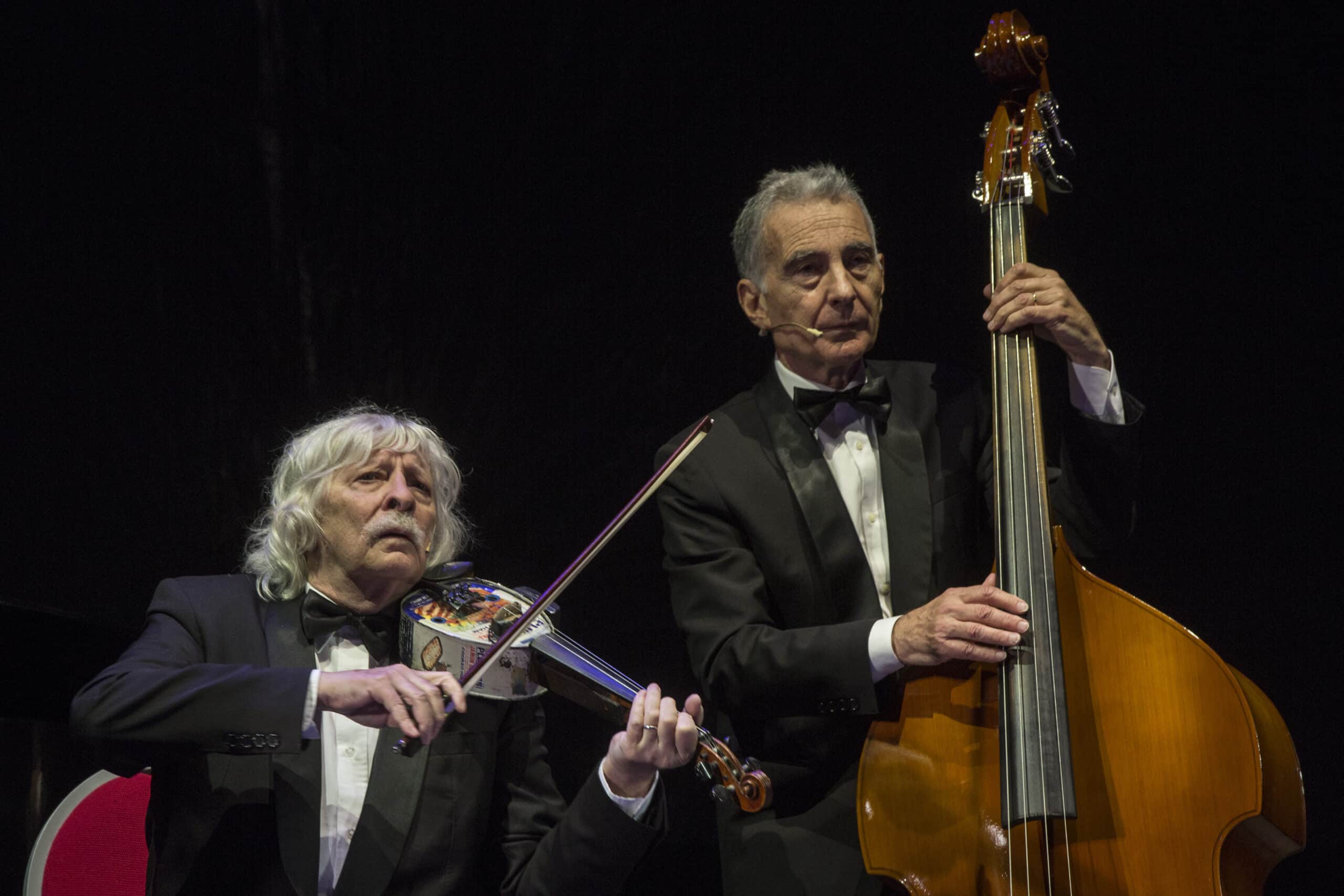 Due componenti di Les Luthiers eseguono un brano con violino di latta e contrabbasso sul palco